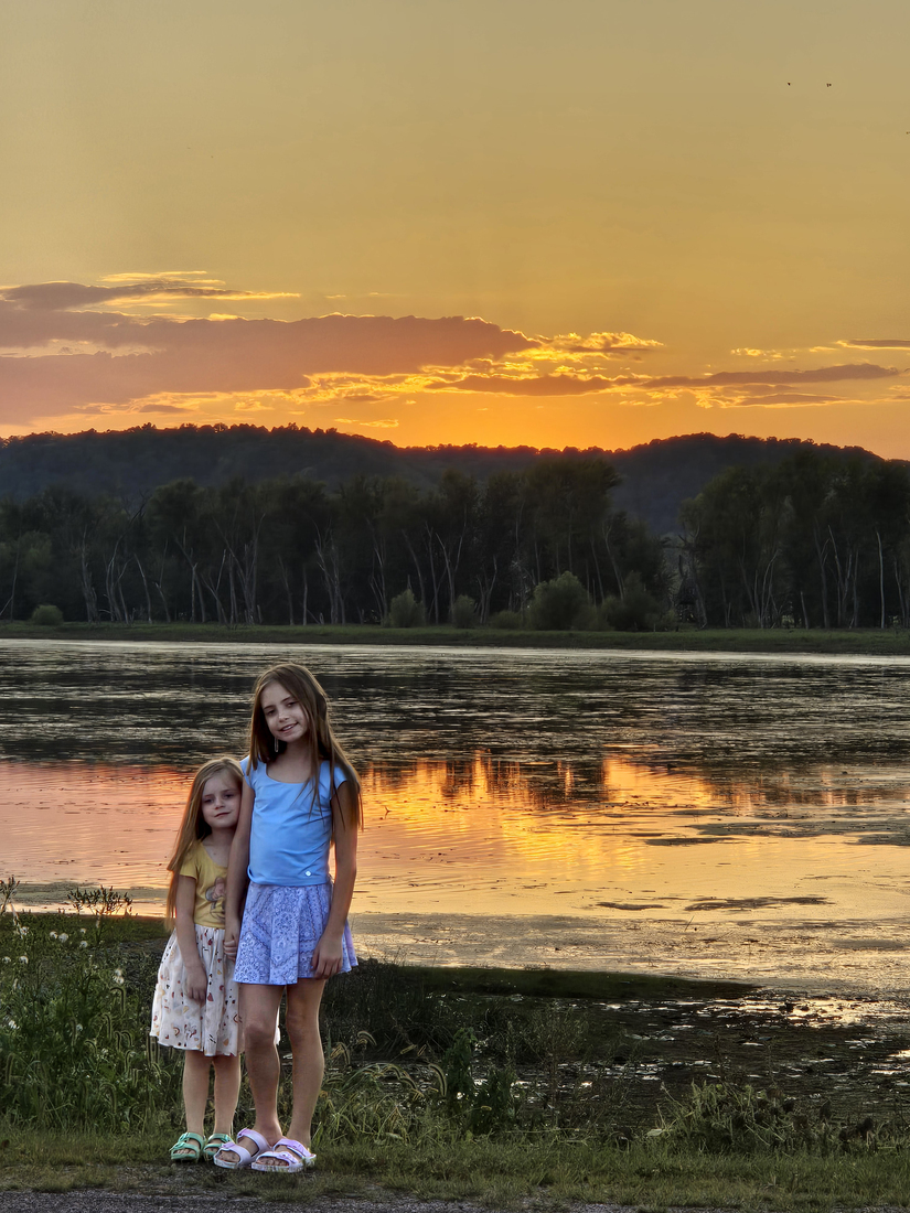 Two girls standing and smiiling with a sunset lake in the background