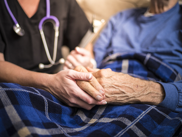 Healthcare worker holding hands of elderly patient