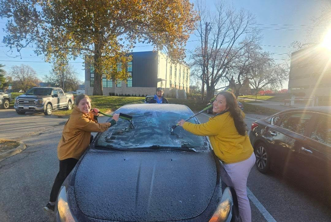 Three residents cleaning frost off a car and smiling at the camera..jpg