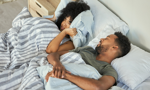 Woman covering ears in bed with snoring partner.jpg