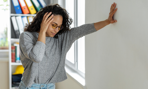 Woman leaning hand on wall and holding head.jpg