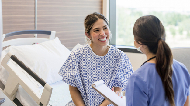 Smiling female patient in hospital gown talking to doctor.jpg