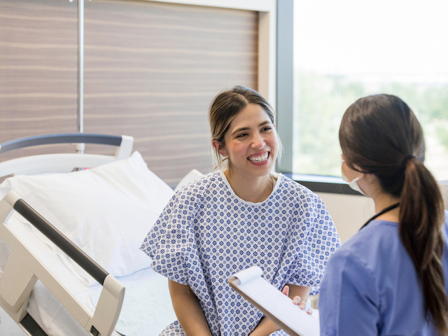Smiling female patient in hospital gown talking to doctor.jpg