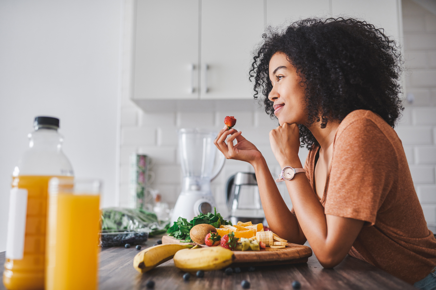 Woman sitting at kitchen table eating a strawberry looking thoughtful
