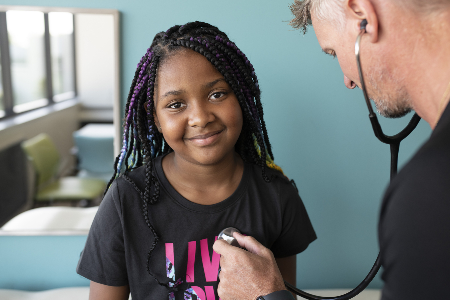 Child smiling as healthcare worker listens to her heart