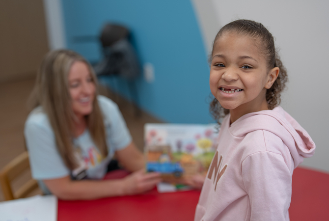 Girl smiling at camera with therapist showing book.jpg