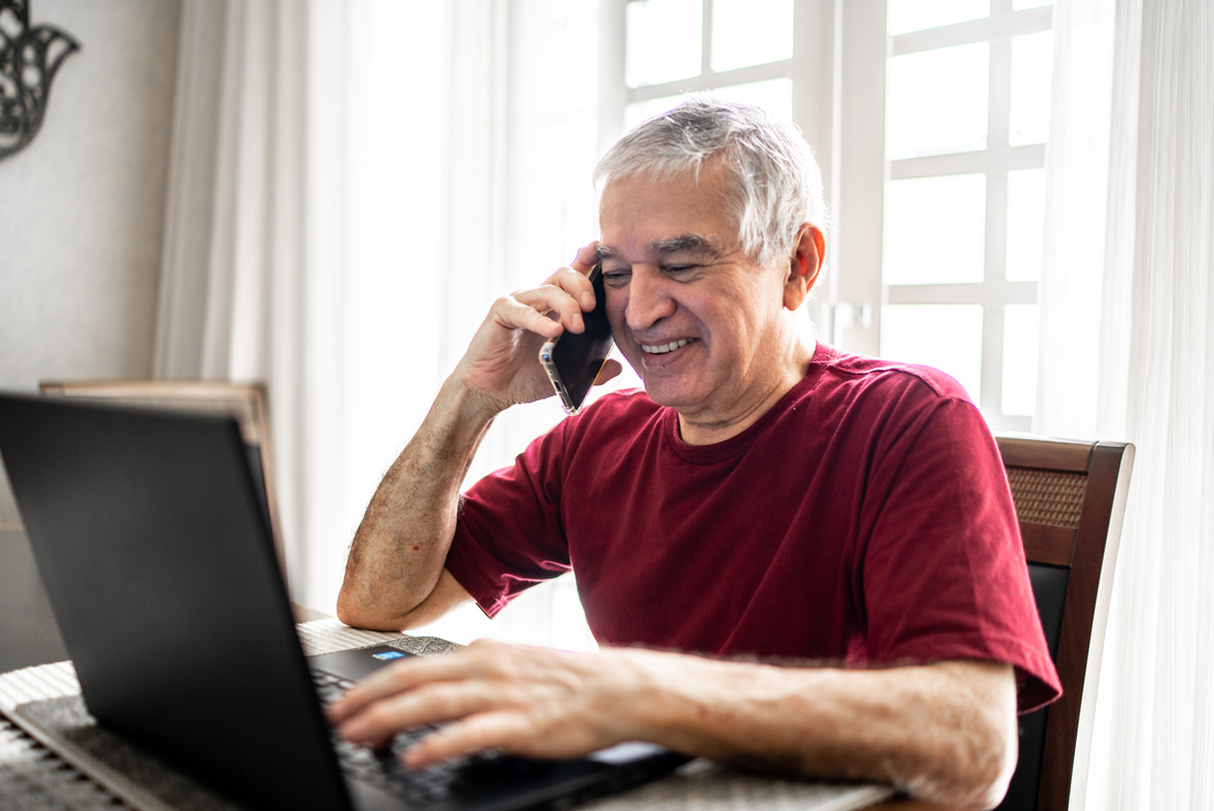 Senior man smiling on phone while using computer.jpg