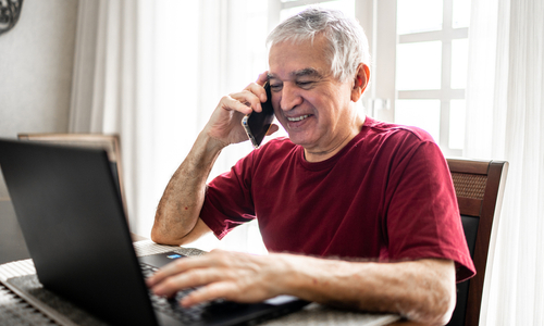 Senior man smiling on phone while using computer.jpg