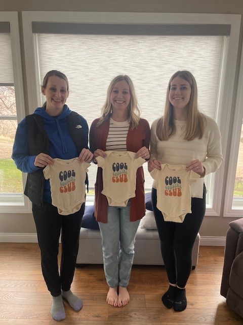 Three Dubuque sisters holding cousin onesies