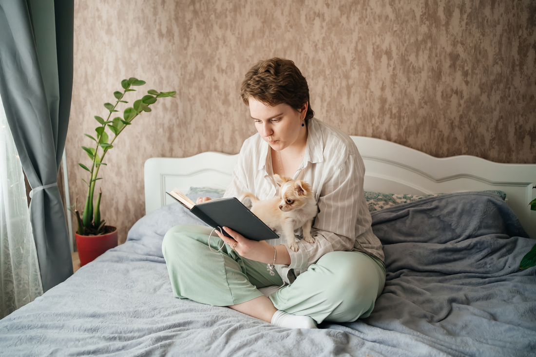 Woman reading a book on a bed with a dog.jpg