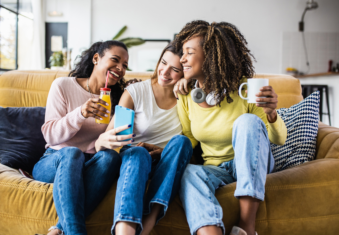 Group of female friends laughing on couch with non-alcoholic drinks