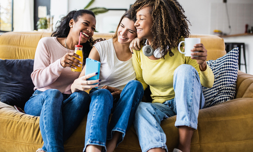 Group of female friends laughing on couch with non-alcoholic drinks
