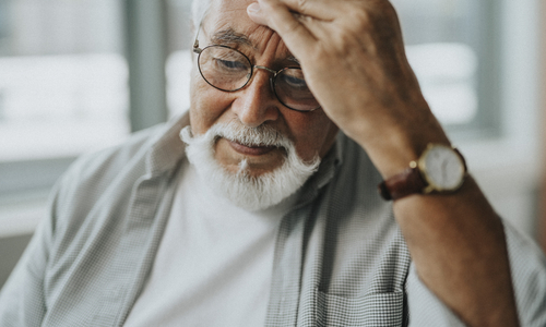 Older adult holding forehead with a headache, illustrating possible warning signs and symptoms of a silent stroke