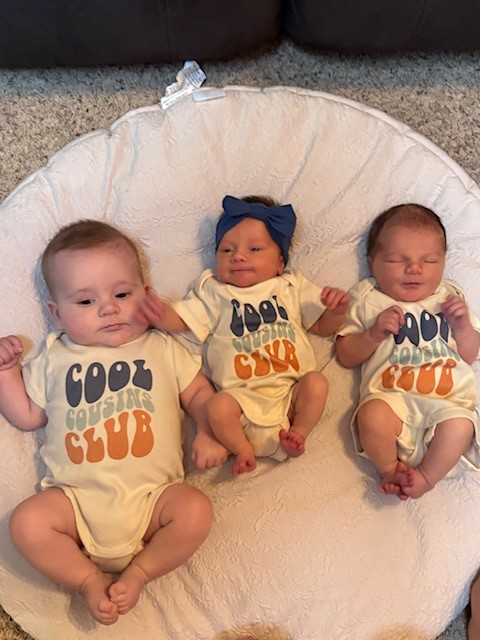 Three babies wearing cousin onesies