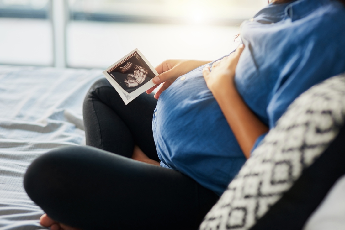 Pregnant woman sitting on bed looking at sonograph